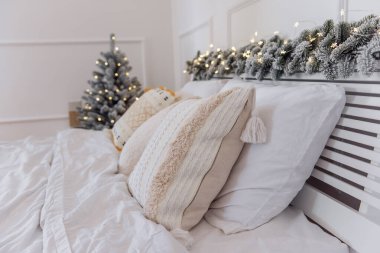 Yeni yıl arifesi. Şenlik yatağında beyaz çarşaflar, süslü yastıklar ve turuncu hardal halısı var. Yatak başlığı yapay karlı dalla süslenmiş. İskandinav moda tasarımı