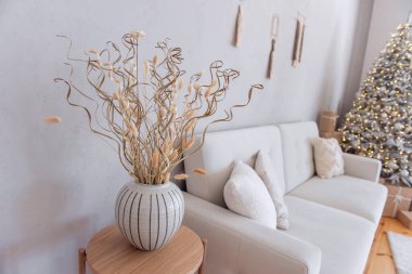 Kurumuş çiçekler, bej vazoda altın dikenler var. Noel ağacının şenlikli arka planı. Şık, modaya uygun İskandinav tarzı, rustik tarzı. Yastıklı modern kanepe. Boşluğu kopyala