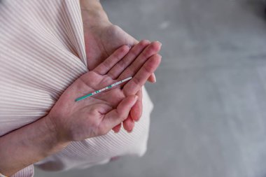 Hamile bir genç kadının elinde iki şeritli bir hamilelik testi var. Sağlıklı, mutlu hamilelikler. Tüplü döllenme. Kısırlığın tıbbi tedavisi. Taşıyıcı annelik. Kapat, boşluğu kopyala