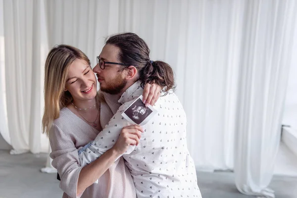 千禧年快乐夫妻拥抱 正在进行超声检查的年轻孕妇 一个留着胡子的男人吻了她心爱的人预产期前的家庭 — 图库照片