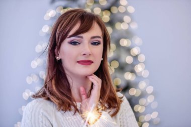 Beyaz örgü kazaklı genç bir kadının portresi Bengal ışığını elinde tutuyordu. Mavi Noel ağacının bulanık arka planında çelenk ışıkları var. Yılbaşı şenliği.