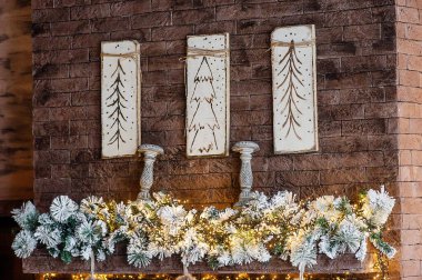 Köknar çelenkli taş bir şöminenin üzerinde Noel çizmeleri. Şamdanlı tuğla duvar. Şenlikli ev dekorasyonu.