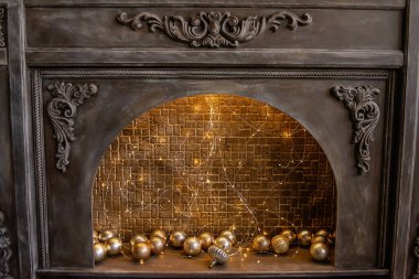 Tuğla duvar, parlak çelenk ve altın Noel toplarıyla süslenmiş eski tahta bir şöminenin sahtesi. İskandinav tarzı bir apartman dairesi. Tatil için şenlik dekorasyonu.