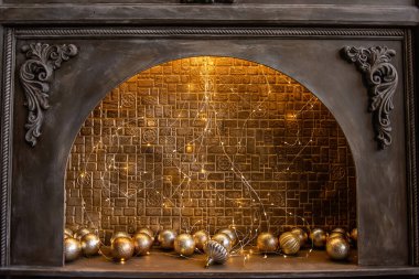 Tuğla duvar, parlak çelenk ve altın Noel toplarıyla süslenmiş eski tahta bir şöminenin sahtesi. İskandinav tarzı bir apartman dairesi. Tatil için şenlik dekorasyonu.