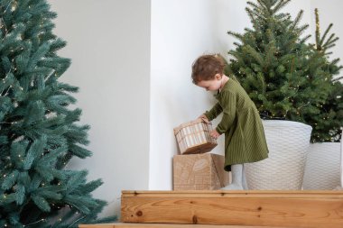 Sıcak yeşil elbiseli küçük kız Noel ağacının yanındaki ahşap merdivenlerde duruyor. Çatı katında hediyelerle kutuları açıyor. Dairenin minimalist İskandinav tarzı. Şenlikli yaşam tarzı