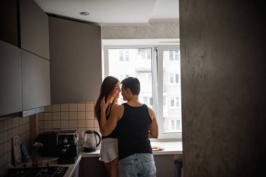 Siyah tişörtlü genç bir çift, sabahları mutfakta pencerede birbirine sarılan kot pantolonlar. Sevgili aşıklar kahvaltıdan önce eğlenirler. Erkekler kadınların saçlarını okşar. Yaşam tarzı apartman hayatı