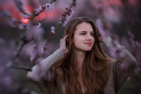 ピンク色の桜の庭の若い千年紀の女性は 赤い太陽の夕日に咲く 柔らかい桃の花で自然の美しさの女の子のクローズアップ肖像画 週末は田舎の街の外を歩く — ストック写真