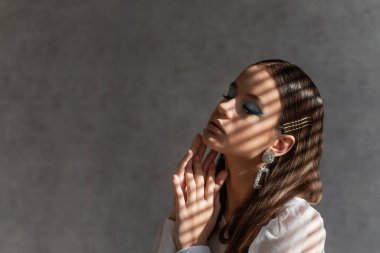 Temiz tenli bir kızın yakın plan güzel portresi. Yüzünde açık renk gölge çizgileri var. Gri dokusal arka plan. Beyaz gömlekli genç bir kadın, gözleri mavi gölgeli bir iş kadını. Boşluğu kopyala