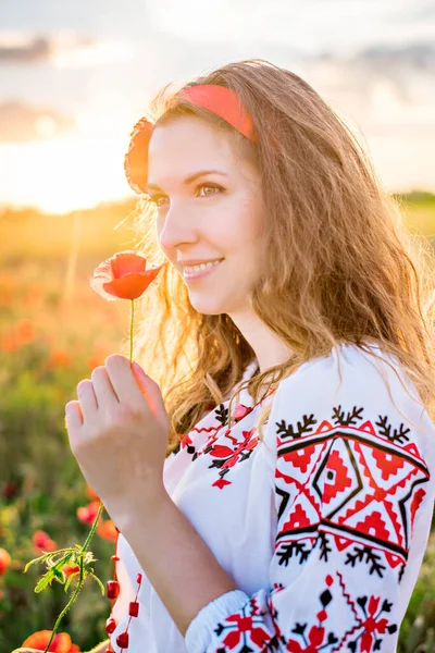フィールド内の若い女性のクローズアップ肖像画 手に赤ケシを保持 民族衣装の少女 頭に花のあるヘッドバンド 刺繍のシャツと赤いスカート 田舎を歩く自然 — ストック写真