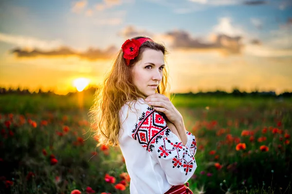 民族ウクライナの衣装刺繍シャツの若い女性のクローズアップ肖像画は日没時に赤いポピーの分野で踊っています 女の子の髪は明るい太陽の光の中で成長します 田舎の週末 — ストック写真