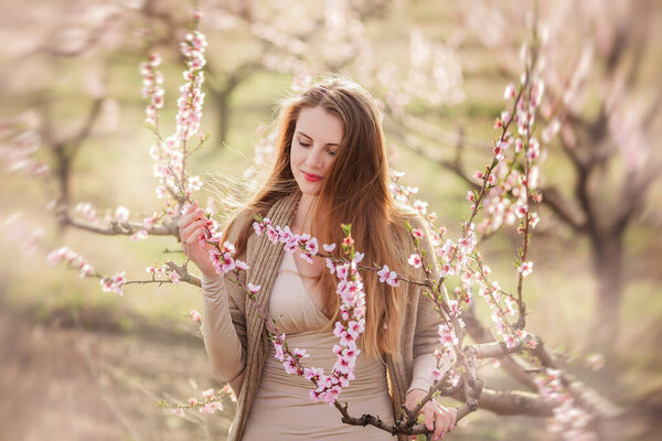 Delicate portrait of a young millennial woman at sunset among flowering trees in blooming gardens. Allergy to flowers. Natural beauty. Beautiful girl in beige dress on botanical background