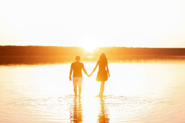 Birbirine aşık bir çiftin silueti. Bir erkek bir kadının elini tutar, turuncu günbatımında gölün sularında yürür. Sevgililer birbirlerine sarılırlar. Yeni evlilerin balayı seyahati. Yeni yaşam konsepti