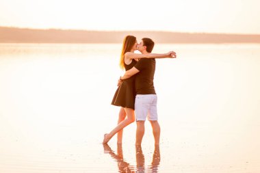 Sevgi dolu bir çift birbirine bakar, sarılır, öper, turuncu günbatımının ışınlarında gölün sularında dururlar. Tutkulu Aşıkların Silueti. Yeni evlilerin balayı seyahati. Hafta sonu dinlenme.