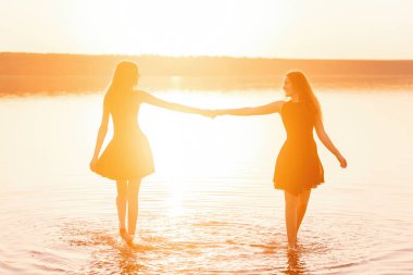 Siyah elbiseli iki kız kardeş gün batımının zıt ışınlarında el ele tutuşarak suyun üzerinde dans ediyorlar. Kızlar yolculukta eğleniyorlar, birlikte daireler çiziyorlar. Kız arkadaşlar denizde dinleniyor.