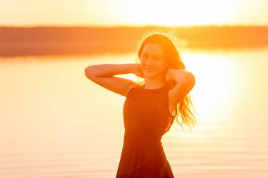 Kıvırcık, özgür bir kızın siluetinin yakın plan portresi, saçlarında rüzgar, turuncu bir günbatımında hafif hareketler. Suda genç bir kadın. Hayat tarzı seyahat hafta sonu. Sağlık, hareket kolaylığı. Boşluğu kopyala