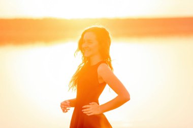 Kıvırcık, özgür bir kızın siluetinin yakın plan portresi, saçlarında rüzgar, turuncu bir günbatımında hafif hareketler. Suda genç bir kadın. Hayat tarzı seyahat hafta sonu. Sağlık, hareket kolaylığı. Boşluğu kopyala