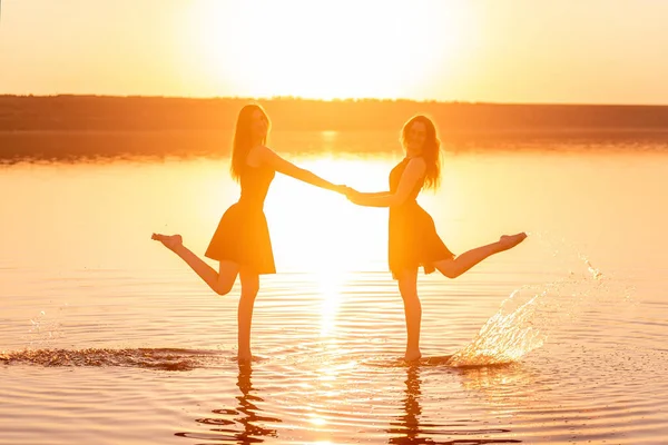 Två Systrar Svarta Klänningar Dansar Vattnet Och Håller Händerna Solnedgångens — Stockfoto