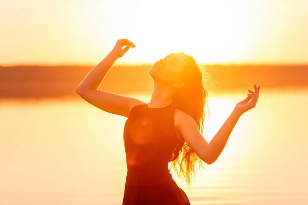 Close-up portrait of silhouette of a curly, free girl, wind in her hair, light movements at an orange sunset. A young woman in the water. Lifestyle travel weekend. Health, ease of movement. Copy space