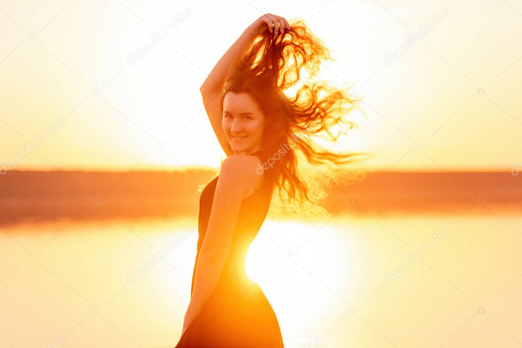 Close-up portrait of silhouette of a curly, free girl, wind in her hair, light movements at an orange sunset. A young woman in the water. Lifestyle travel weekend. Health, ease of movement. Copy space
