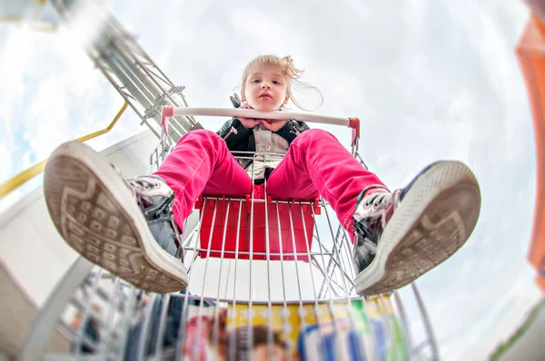 Küçük kız alışveriş arabasında otururken eğleniyor. Çocuk ailesiyle birlikte ticaret merkezine alışverişe gitti. Kız oynaşıyor, farklı duygular yaratıyor, dilini gösteriyor, at arabasına biniyor.