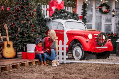 Beyaz anne sarılıyor, Afro-Amerikan oğlunu öpüyor, Noel ağacının yanında oturuyor, beyaz bir çitin arkasında, kırmızı bir araba. Genç kadın, Noel Baba 'nın hediyelerini açan çocuğun kafasını okşuyor. İyi tatiller.