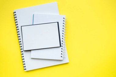 Blok yığını ve spiral kaplı defterler. Parlak sarı arka plan. Uzayı kopyala Üst manzara, düz yatış. Okul konseptine dönelim..