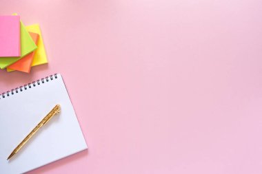 Bir tarafında altın kalem ve yapıştırma yığını olan defter. Fotokopi alanı. Açık renkli, pembe arkaplan. Üst manzara, düz yatış. Okul konseptine dönelim..