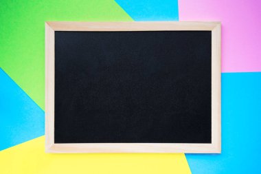 Empty chalkboard on line of pink, yellow, green and light blue paper background. Back to school or schools out concept. Copy space, top view
