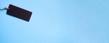 İpin üzerinde boş bir siyah kağıt fiyat etiketi olan pankart. Açık mavi arkaplan. Boşluğu kopyala, üst görünüm.