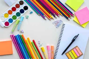 Açık gri arka planda kalemler, boyalar, keçeli kalemler ve diğer okul kağıtları. Üst görünüm, düz görünüm, kopyalama alanı