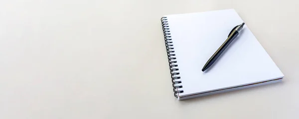 Banner with copy space. Notebook on a spiral on a plain beige background. Blank white sheets in a note. Flat lay, top view.