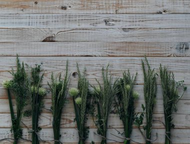 Köyün çiçekli geçmişi. Çimen, soğan çiçeği ve kişniş demetleri ahşap beyaz arka planda serilmiştir..