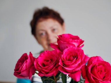 Arka plan bulanık. Evde elinde bir buket çiçekle güzel bir son sınıf öğrencisi var. Geçmişi bulanık. Anneler Günün kutlu olsun. Her yaşta güzellik.