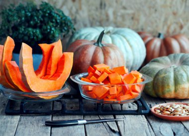 Tahta eski bir masada dilimlenmiş balkabağı meyvesi. Tencereye konmuş balkabağı parçaları, haşlanmaya hazır. Ön planda kabak çekirdekleri var. Yakın plan fotoğraf. Şeker hastalarının ve diyetçilerin beslenmesi için faydalı bir ürün..