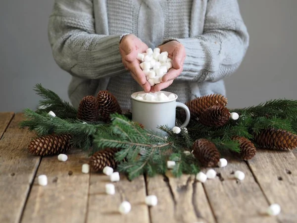 Branche de sapin, mini guimauves dans une tasse de cacao, une bougie allumée sur le fond d'une table rustique en bois et les mains d'une femme âgée. — Photo