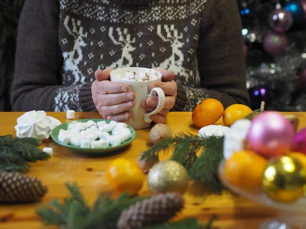 Les mains tiennent une tasse de guimauves et de cacao chaud sur une table avec des branches d'épinette parmi les mandarines et les décorations d'arbres de Noël. Noël, vacances d'hiver et de loisirs et de loisirs concept. — Photo