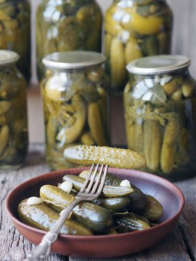 Konserve salatalık turşusunun faydaları ve zararları. Çatal üzerinde ev yapımı salatalık turşusu ve tahta bir arka planda kavanozlar. Yan görüş. Metin için yer.