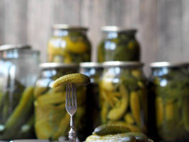 Konserve salatalık turşusunun faydaları ve zararları. Çatal üzerinde ev yapımı salatalık turşusu ve tahta bir arka planda kavanozlar. Yan görüş. Metin için yer.