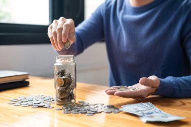 Genç adam para biriktirmek için şişeye para koyuyor. İleride seyahat, eğitim, ev ve emeklilik için para kutusu stratejisi oluşturacak..