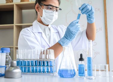 Laboratuvarda virüs ve aşı antiretroviral koronavirüs hakkında çalışan kadın araştırmacı ya da doktor test tüpleri ve mavi sıvı çözeltisi ile araştırma yapıyor..