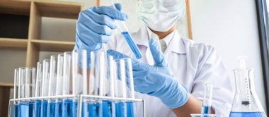 Laboratuvarda virüs ve aşı antiretroviral koronavirüs hakkında çalışan kadın araştırmacı ya da doktor test tüpleri ve mavi sıvı çözeltisi ile araştırma yapıyor..
