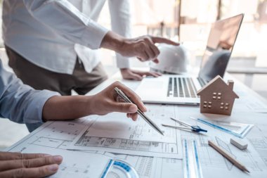 Mimarlar veya mühendislik ekibi, modern ofisteki tasarım ve model ev üzerine yeni mimari projeler planlayan nesneler, araçlar ve inşaat çizimleri üzerinde danışmanlık ve analiz yapıyor..