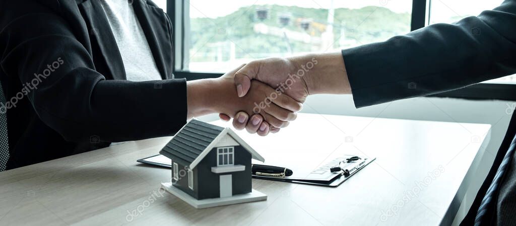 Estate agent and client are shaking hands after good deal home loan after discussing and signing contract to rent a house with approved insurance form.