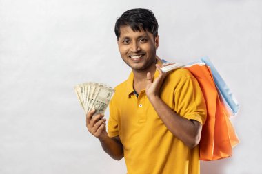 Beyaz arka planda kameraya gülümseyen sarı elbiseli ve Hint paralı orta yaşlı bir Hintli.