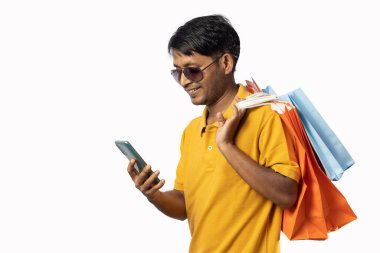 Beyaz arka planda kameraya gülümseyen sarı elbiseli ve akıllı telefonlu orta yaşlı bir Hintli.