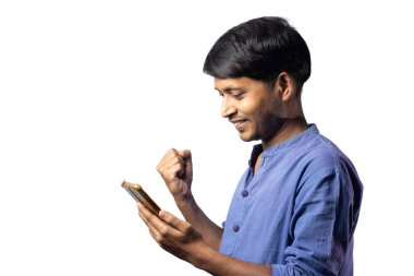 Mavi elbiseli genç Hintli bir erkek beyaz arka planda cep telefonuyla yumruğunu gösteriyor.