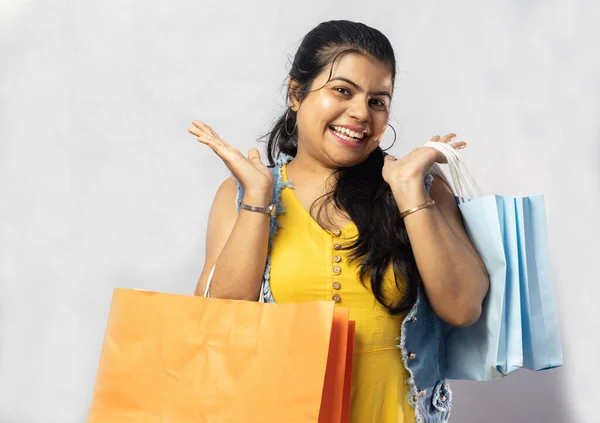 白い背景にカメラを見てショッピングバッグと黄色のドレスの美しいインド人女性 — ストック写真