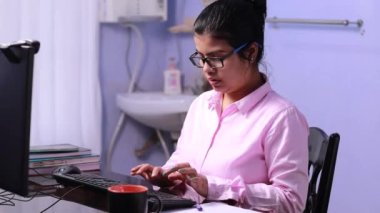 Pembe elbiseli Hintli kadın bilgisayarla çalışıyor ve evde notlar alıyor.