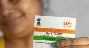 Birbhum, Batı Bengal / Hindistan - 21 Aralık 2021: Gülen yüzlü genç Hintli bir kadının elinde tuttuğu Aadhaar kartı üzerine seçici odaklanma