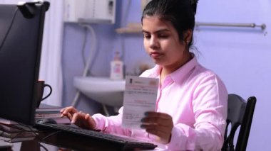 Pembe elbiseli Hintli kadın evde bilgisayarında aadhaar kartıyla çalışıyor.